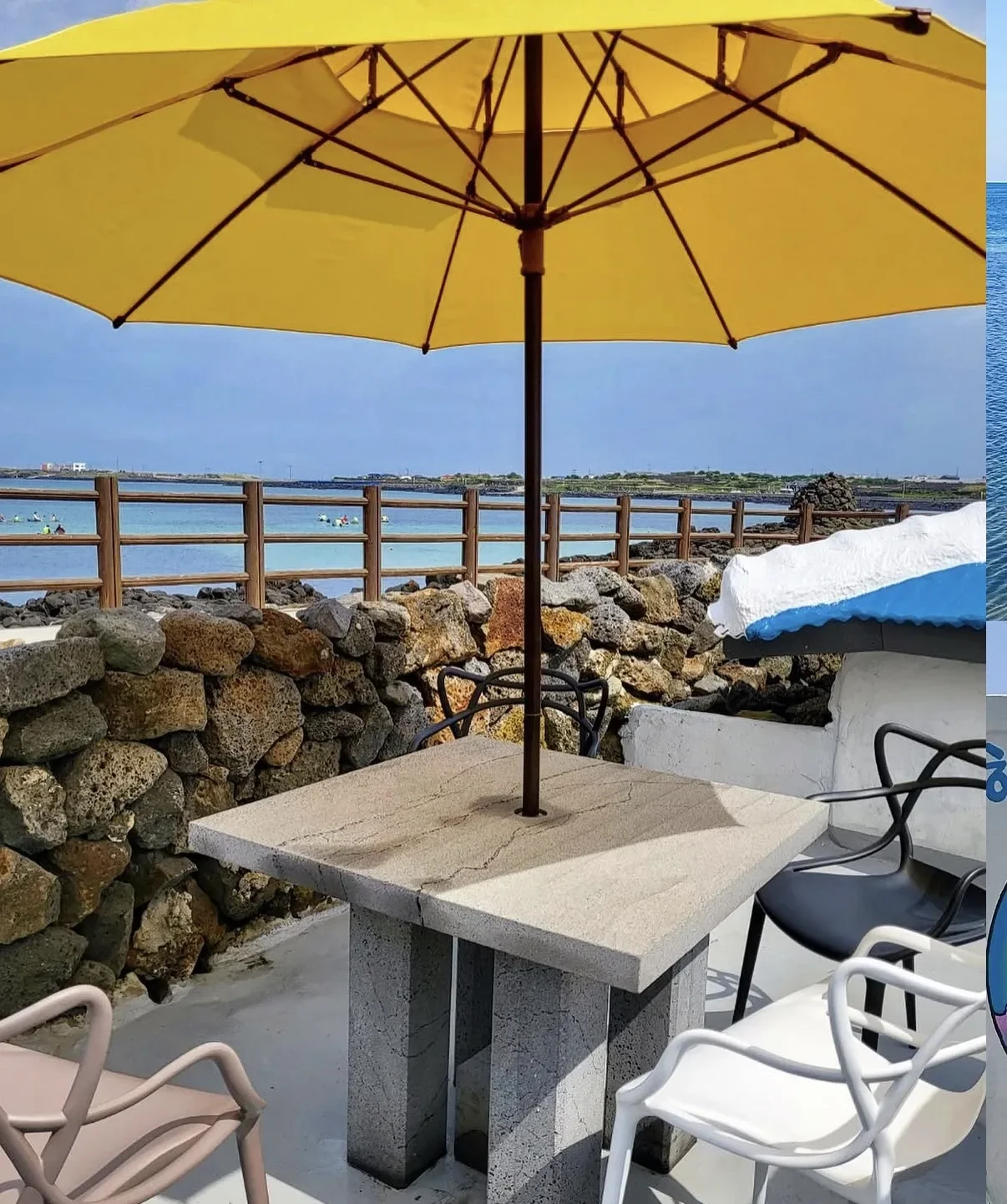 Seaside café terrace on Udo with a stone table under a yellow parasol, a low black stone wall and turquoise sea beyond